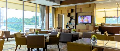 Una habitación de hotel moderna con un ventanal grande, un sofá, una mesa de comedor y un televisor.