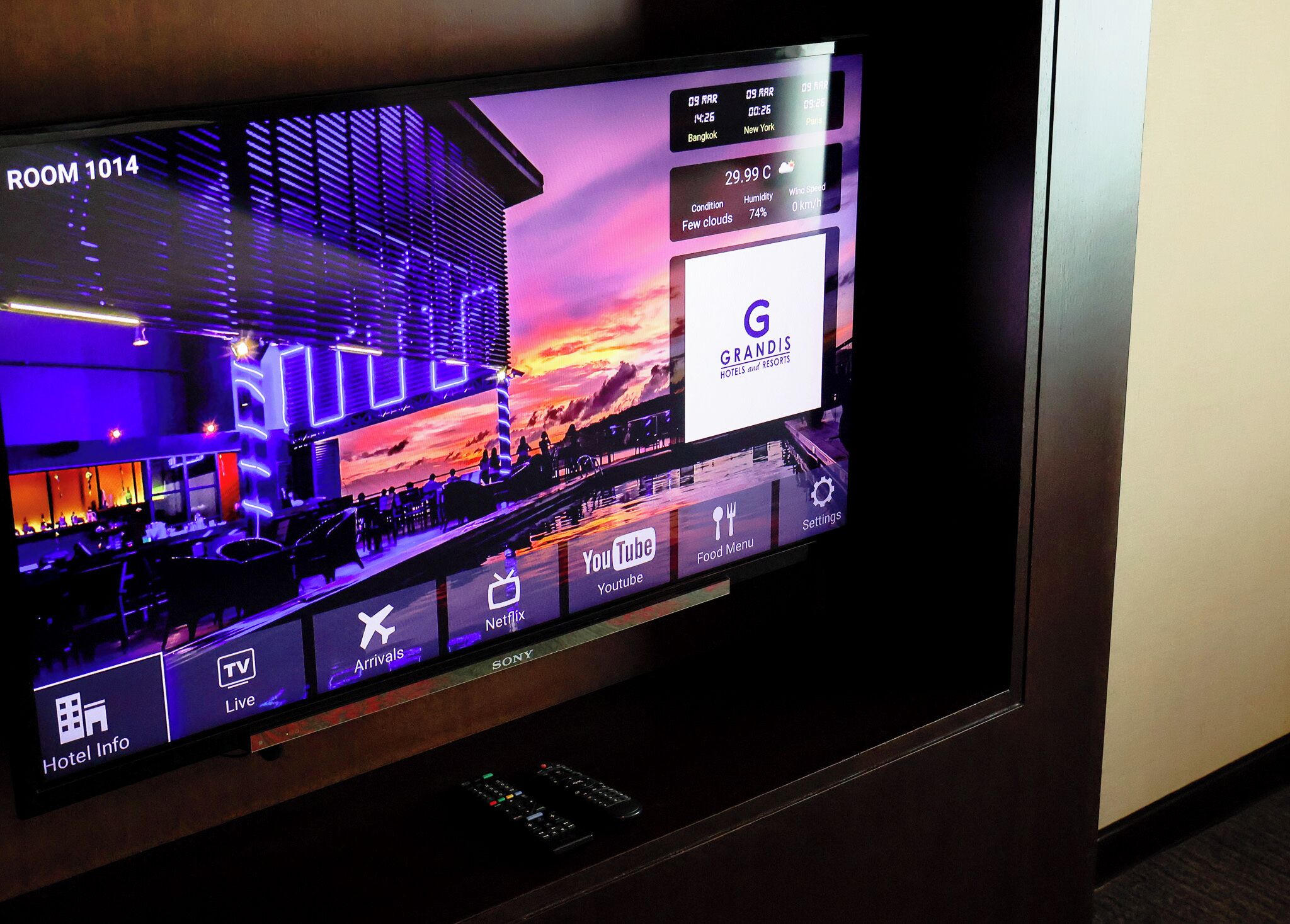 A hotel room with a large flat-screen TV displaying a hotel information interface, including room number, amenities, and a view of the hotel's exterior.
