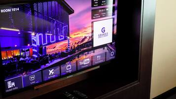 A hotel room with a large flat-screen TV displaying a hotel information interface, including room number, amenities, and a view of the hotel's exterior.