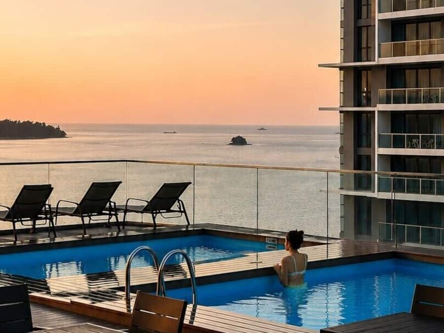 Zona de piscina con sillones de descanso y vista al mar al atardecer.
