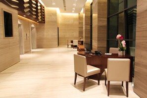 A modern hotel lobby with a reception desk, two chairs, a small table, and a potted plant. - Grandis Hotel (Kota Kinabalu)