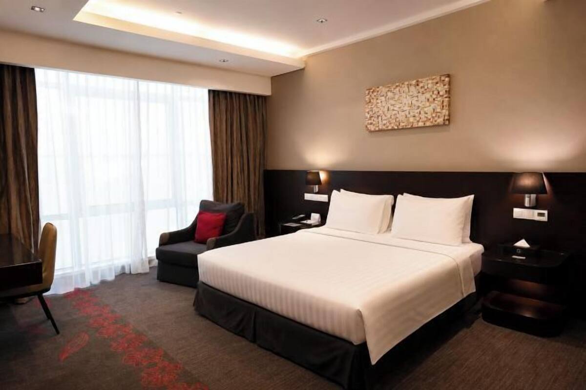 A hotel room with a large bed, a desk, a chair, and a nightstand.