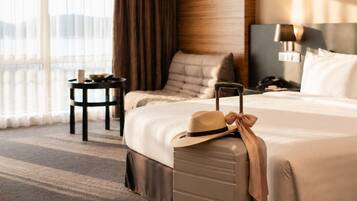 Habitación de hotel con una cama grande, una maleta, una mesita de noche y vistas al exterior.