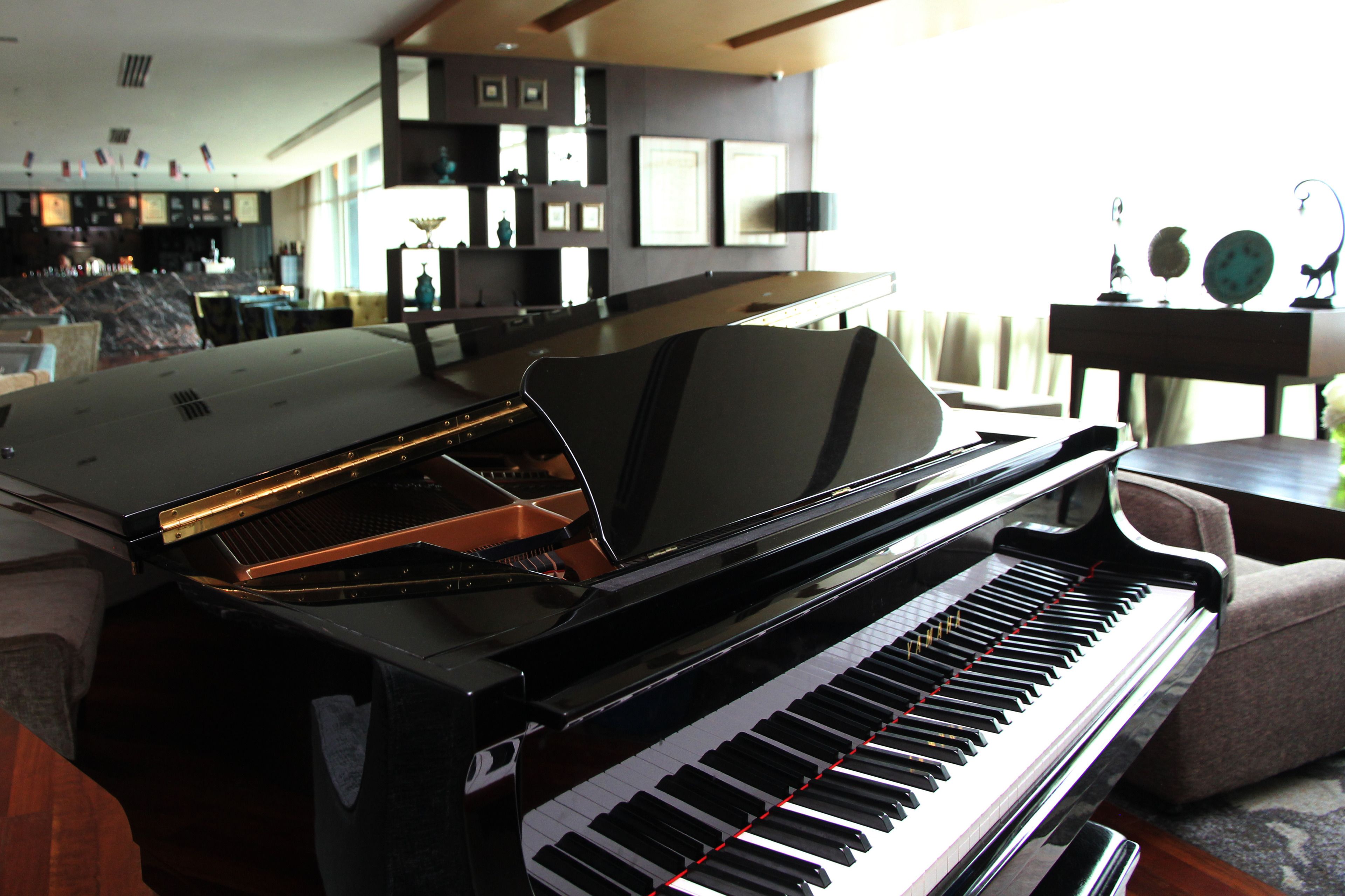 A grand piano in a well-lit living room with a modern interior design, including a bar area in the background.