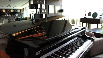 A grand piano in a well-lit living room with a modern interior design, including a bar area in the background.