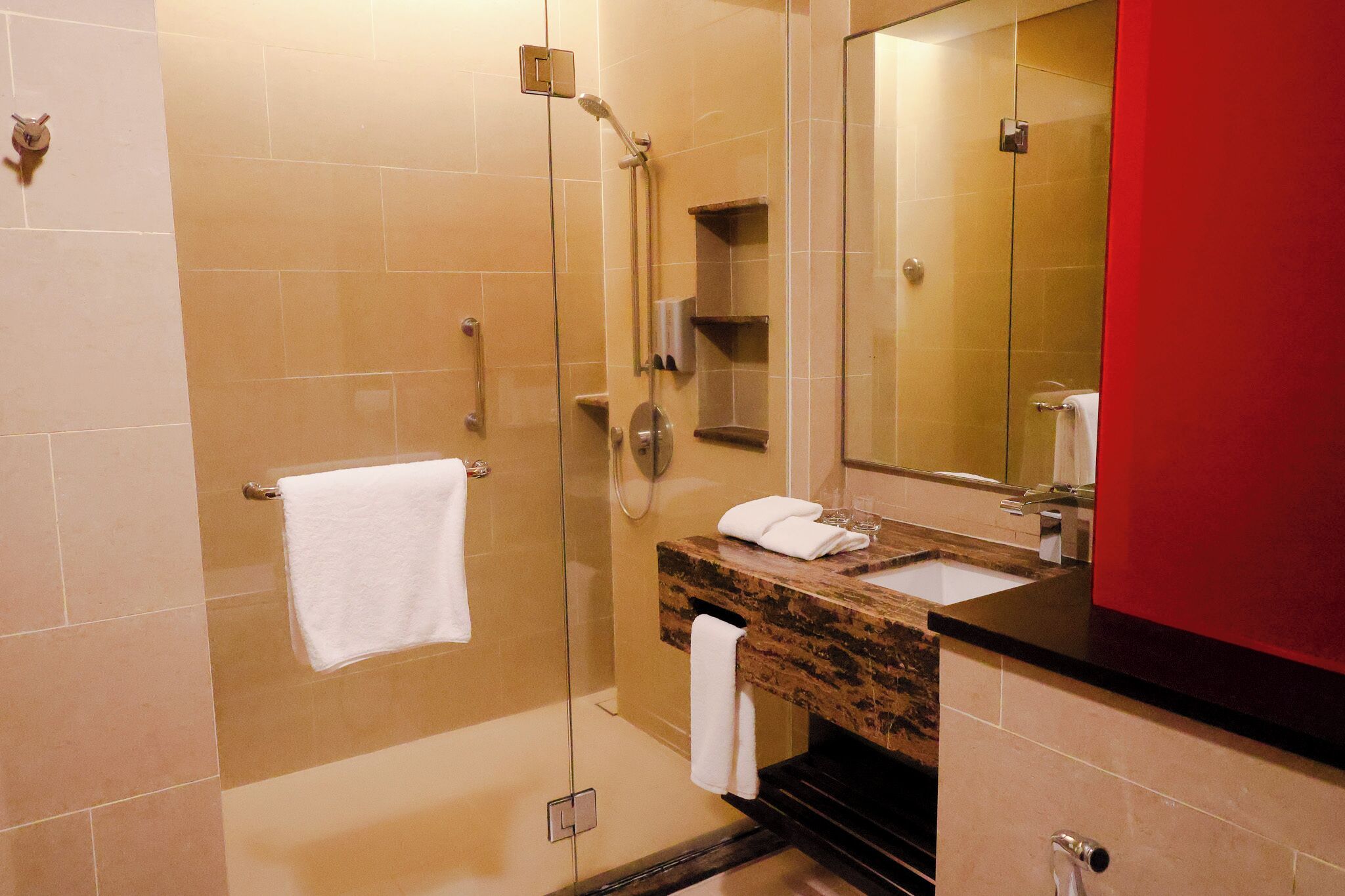 Een badkamer met een douche met glazen wanden, een wastafel met een marmeren blad en een spiegel.