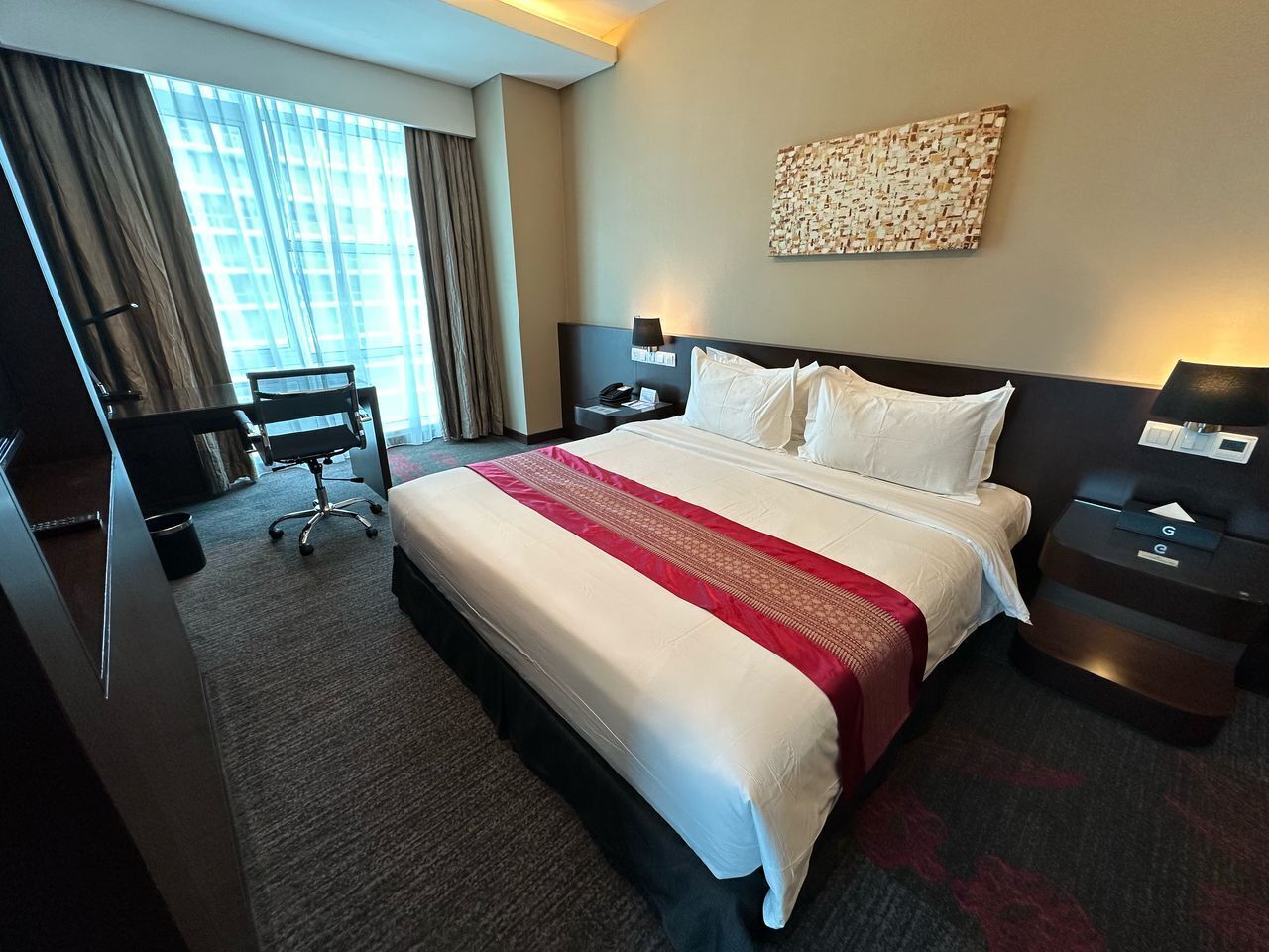 A hotel room with a large bed, a desk, a chair, and a window with curtains.
