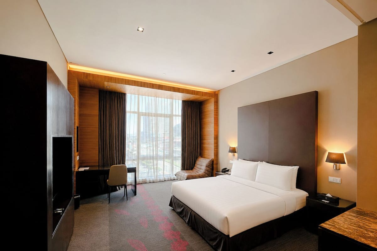 A hotel room with a large bed, a desk, a chair, a TV, and a window with curtains.