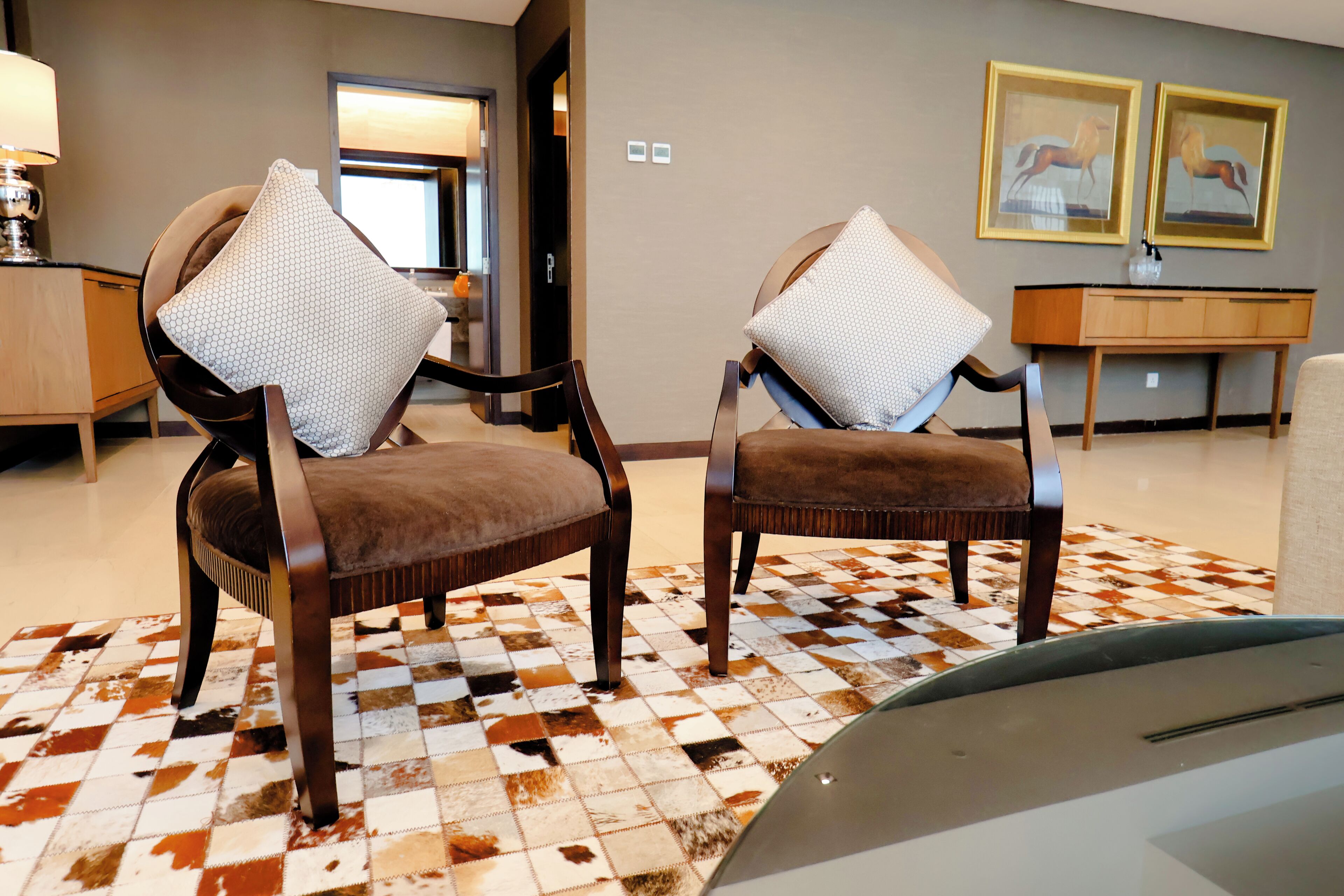 Quarto com duas poltronas estofadas, tapete estampado, mesa consola de madeira e quadros nas paredes.