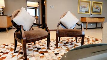 Quarto com duas poltronas estofadas, tapete estampado, mesa consola de madeira e quadros nas paredes.