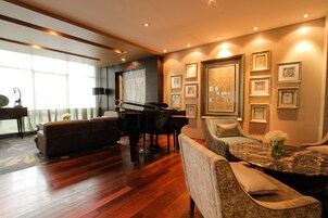 A spacious living room with a grand piano, comfortable seating, and a large window providing natural light.