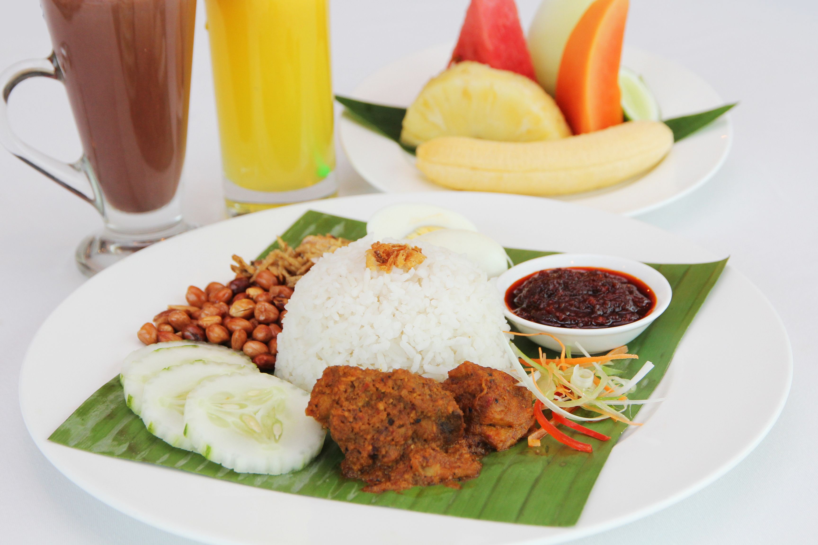 A plate of food with rice, peanuts, cucumber slices, and a fried item, served on a banana leaf.