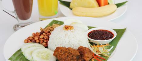 A plate of food with rice, peanuts, cucumber slices, and a fried item, served on a banana leaf.