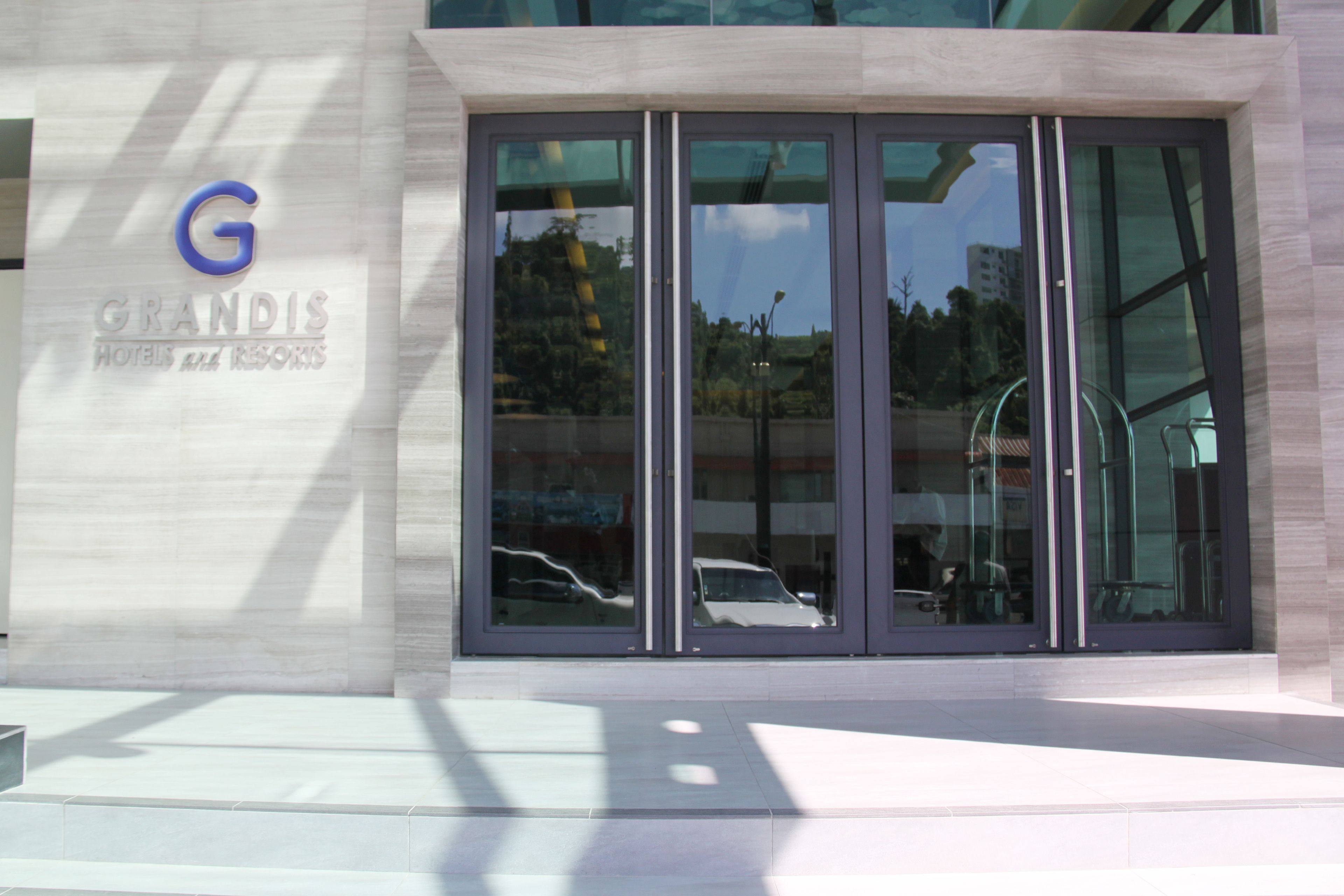 L'ingresso moderno di un hotel con facciata in vetro, un logo 'G' ben visibile e un cartello che recita 'GRANDIS HOTELS & RESORTS'.