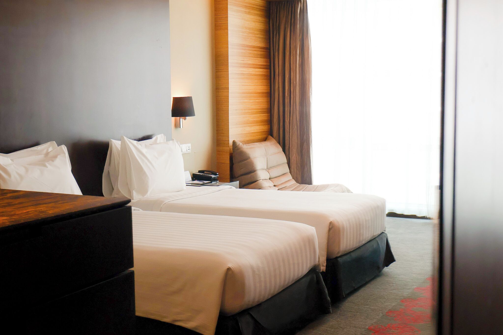 A hotel room with two beds, a desk, a lamp, and a view of the outdoors.