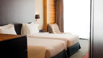 A hotel room with two beds, a desk, a lamp, and a view of the outdoors.