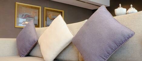A sofa with multiple cushions, a framed picture on the wall, and two white vases on a table.
