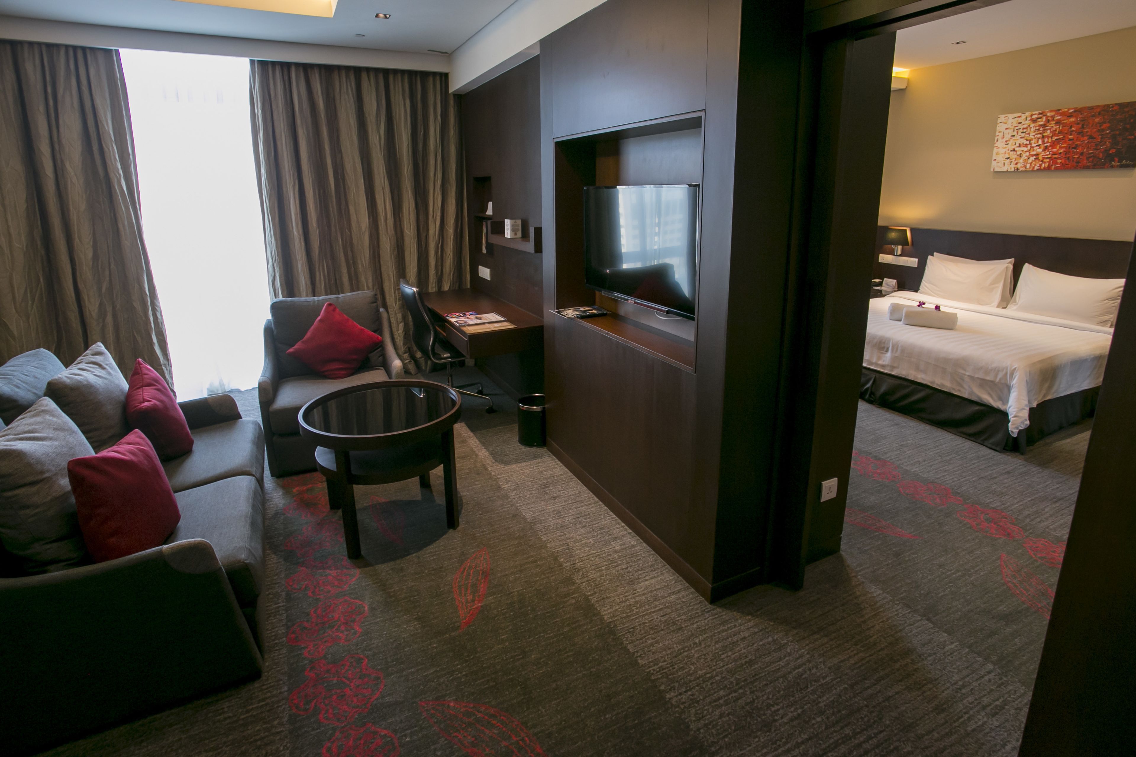 A hotel room with a sofa, a small table, a TV, a bed, and a carpet with a leaf pattern.