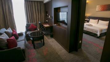 A hotel room with a sofa, a small table, a TV, a bed, and a carpet with a leaf pattern.