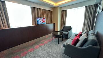 Una habitación de hotel con sofá, sillón, una mesita y televisor montado en la pared.