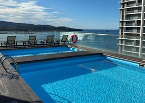 Zona de piscina con sillas de descanso y un flotador salvavidas, con vista a una masa de agua y una tierra lejana.