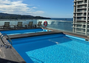 Zona de piscina con sillas de descanso y un flotador salvavidas, con vista a una masa de agua y una tierra lejana.