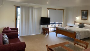 A hotel room with a bed, a TV, a balcony with a table and chairs, and a sofa. - Marsden Court Apartments (Strahan)