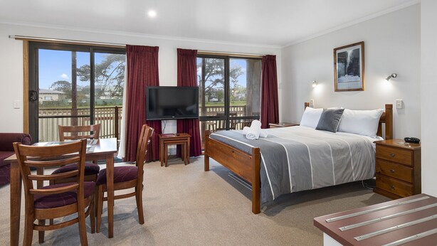 A bedroom with a bed, a TV, a desk, and chairs. - Marsden Court Apartments (Strahan)