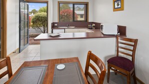 A compact kitchen with a dining area, a microwave, and a window with blinds. - Marsden Court Apartments (Strahan)