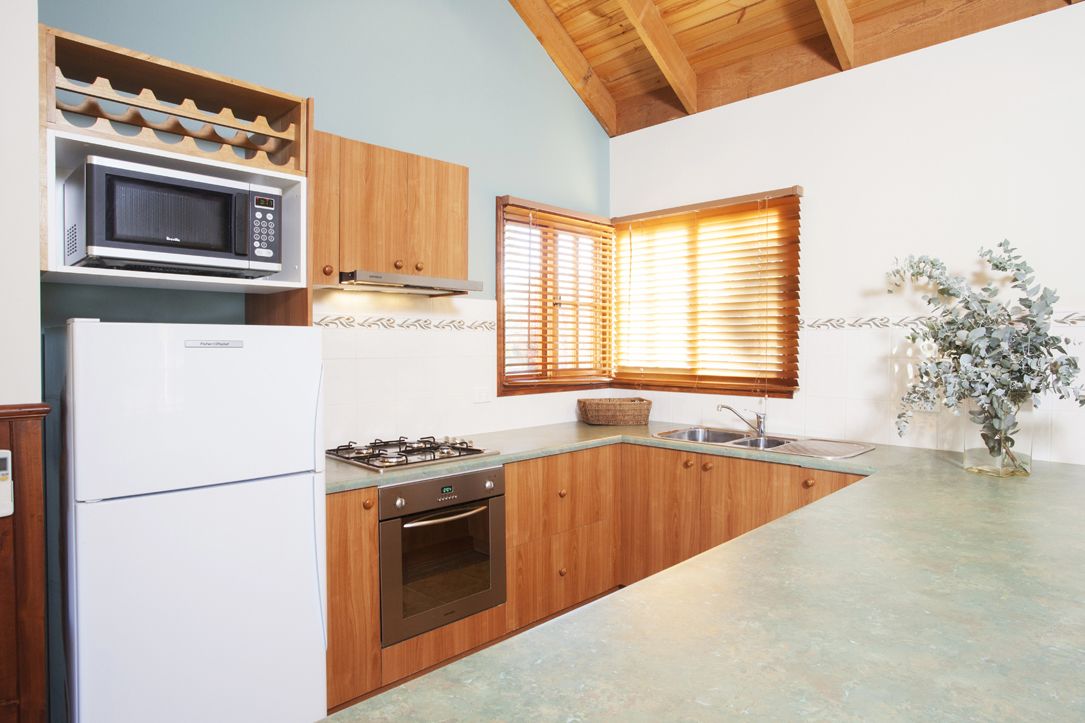 A kitchen with wooden cabinets, a built-in microwave, a refrigerator, a stove, and a window with blinds.