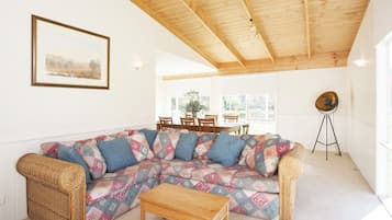 Ein gemütliches Wohnzimmer mit Holzboden, einem gemusterten Sofa, einem kleinen Holztisch und einer Dreibeinlampe.