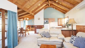 Ein gemütliches Wohnzimmer mit Holzbalkendecke, einer Sofagarnitur, einem Couchtisch und einer Küche im Hintergrund.