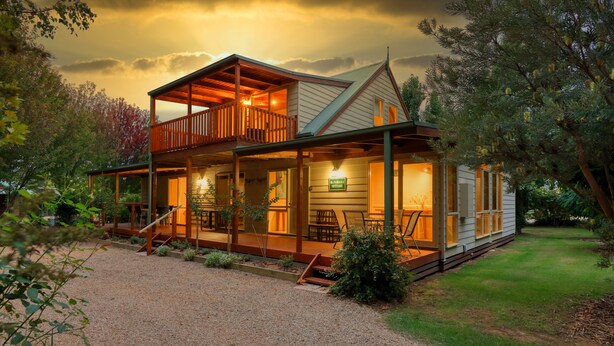 Ein zweistöckiges Cottage mit Balkon, überdachter Veranda und Kiesweg.