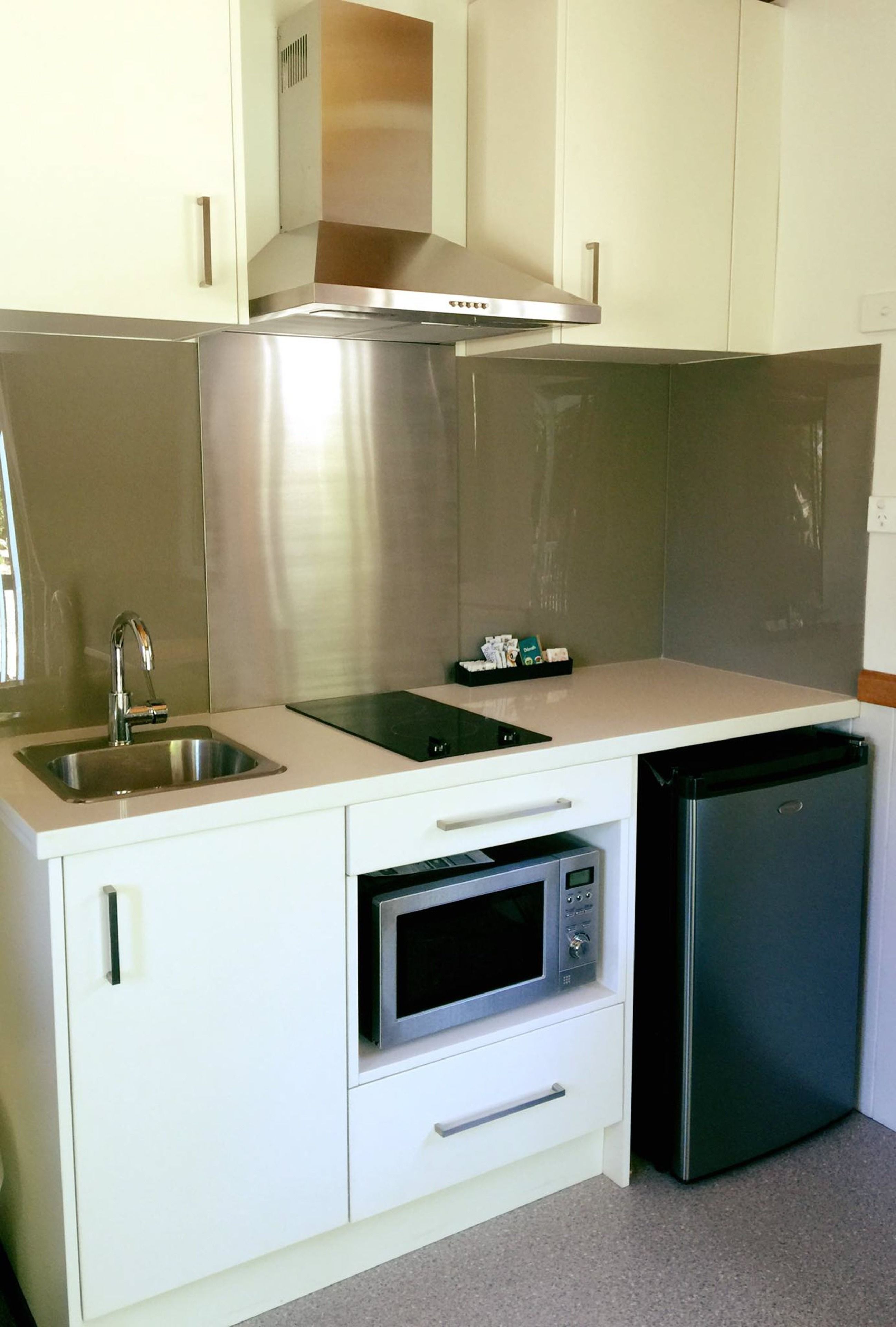 A compact kitchen with a stainless steel range hood, a built-in microwave, and a black refrigerator.