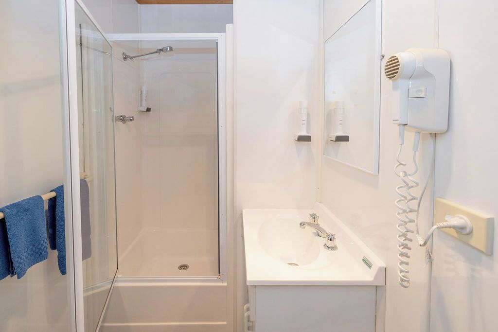 A bathroom with a glass-enclosed shower, a white sink, and a hairdryer mounted on the wall.