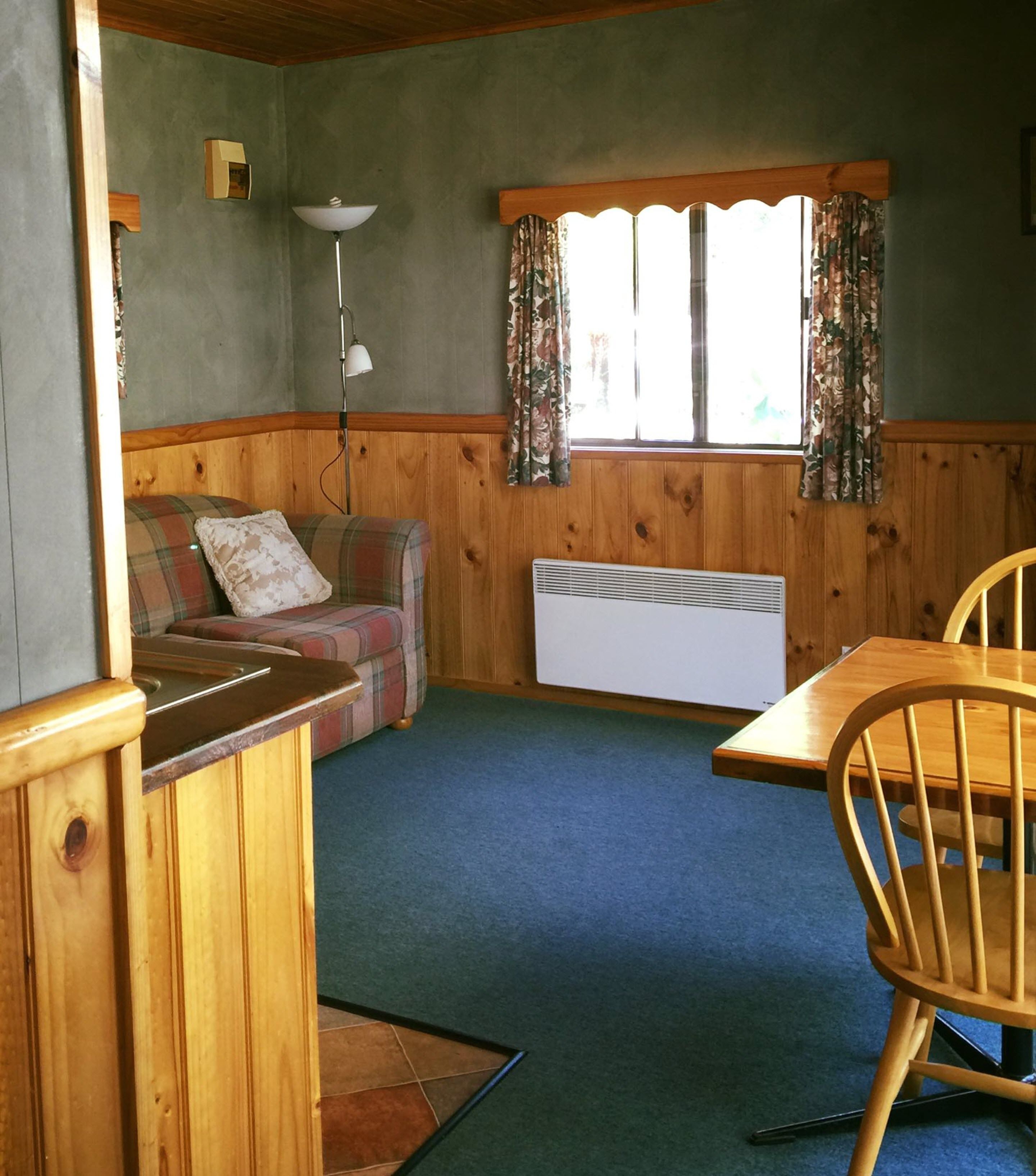 Una habitación acogedora con un banco de madera, un sofá a cuadros, una mesa y una ventana con cortinas.