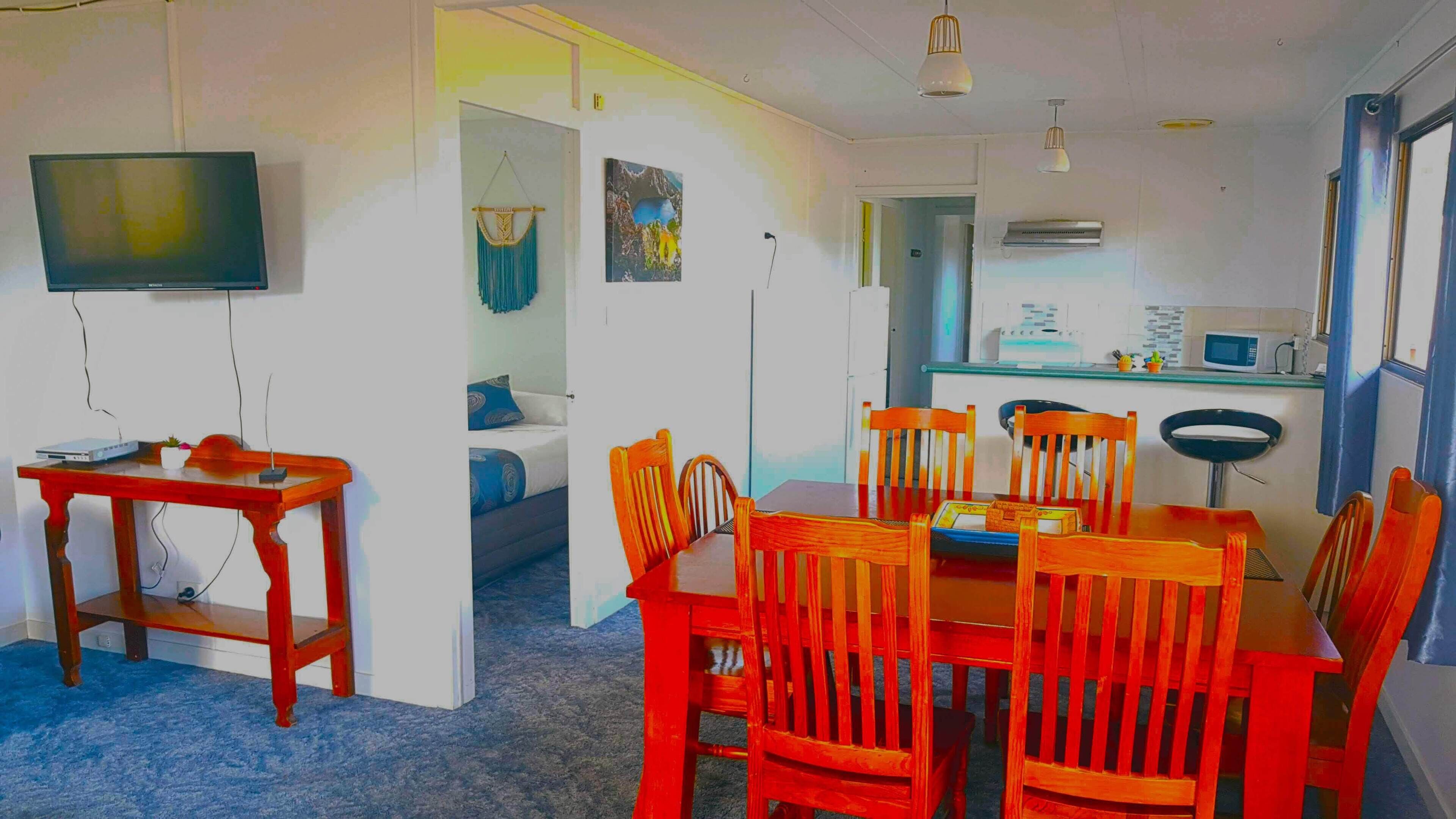 A compact living space with a dining area, kitchenette, and a TV mounted on the wall.