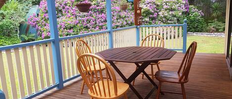 A wooden deck with a table and chairs, surrounded by a blue railing and vibrant pink flowers.