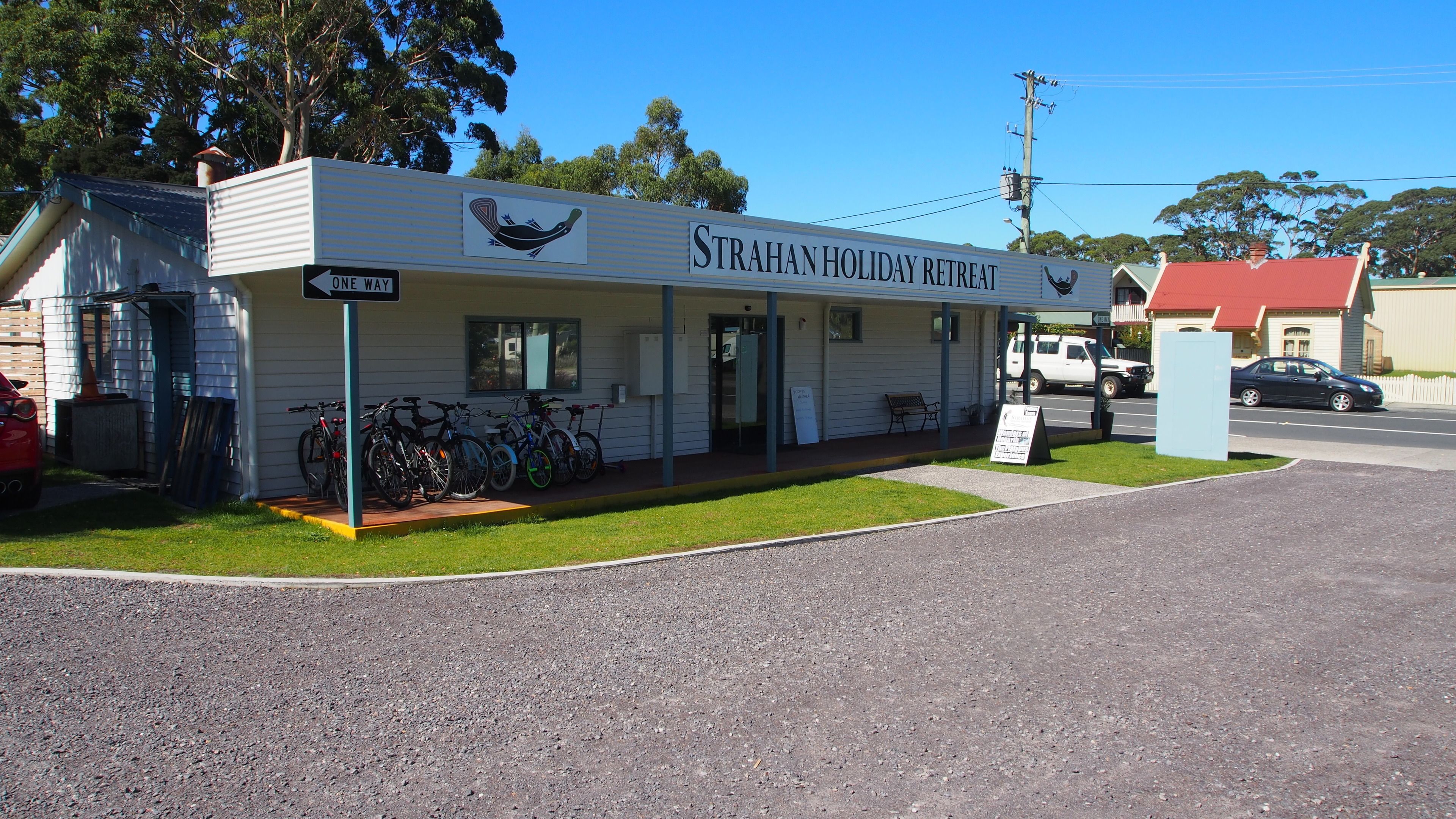 A building labeled "Strahan Holiday Retreat" with a one-way sign, bicycles parked outside, and a grassy area in front.