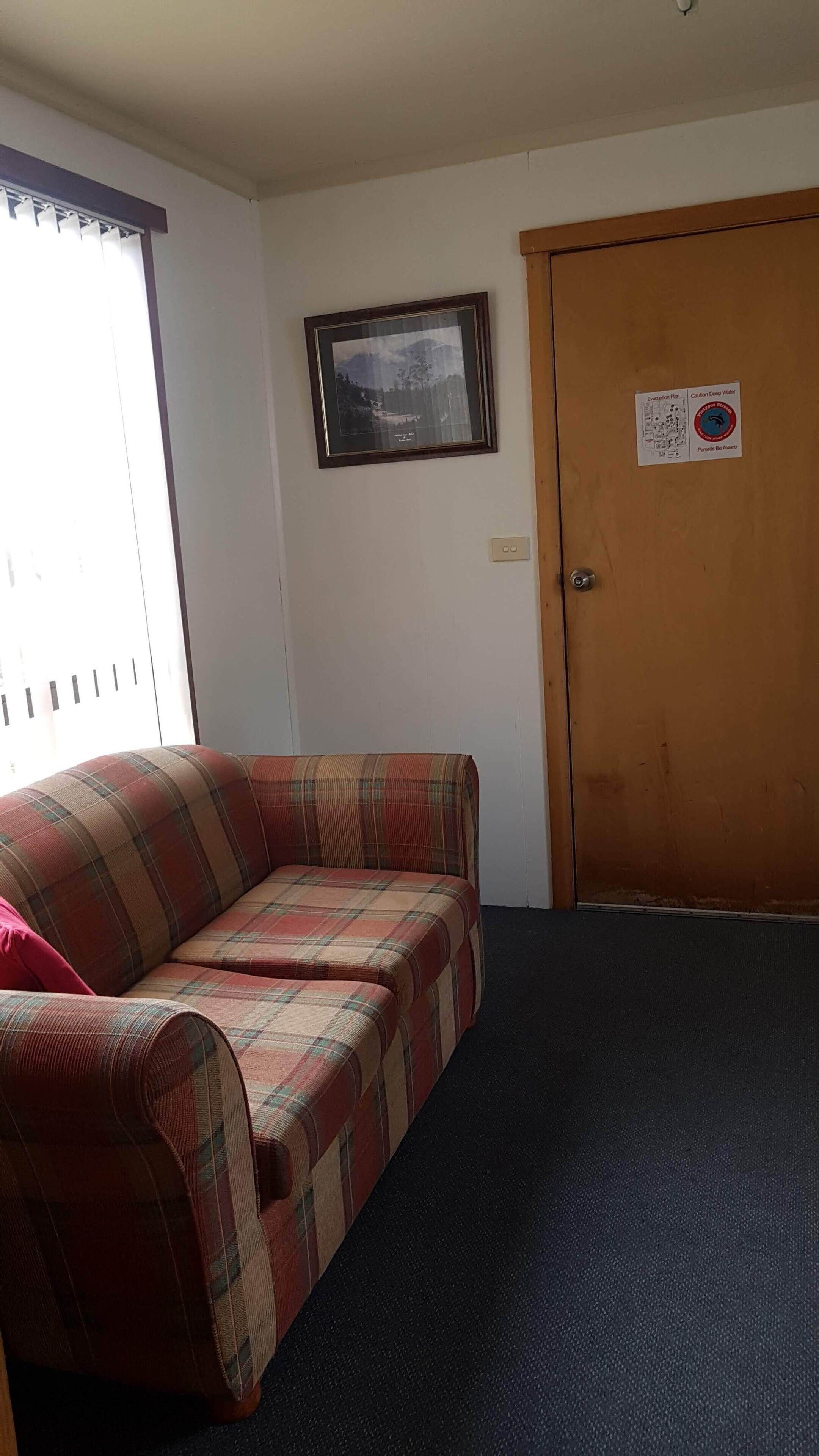 A room with a plaid sofa, a framed picture on the wall, and a door with a caution sign.