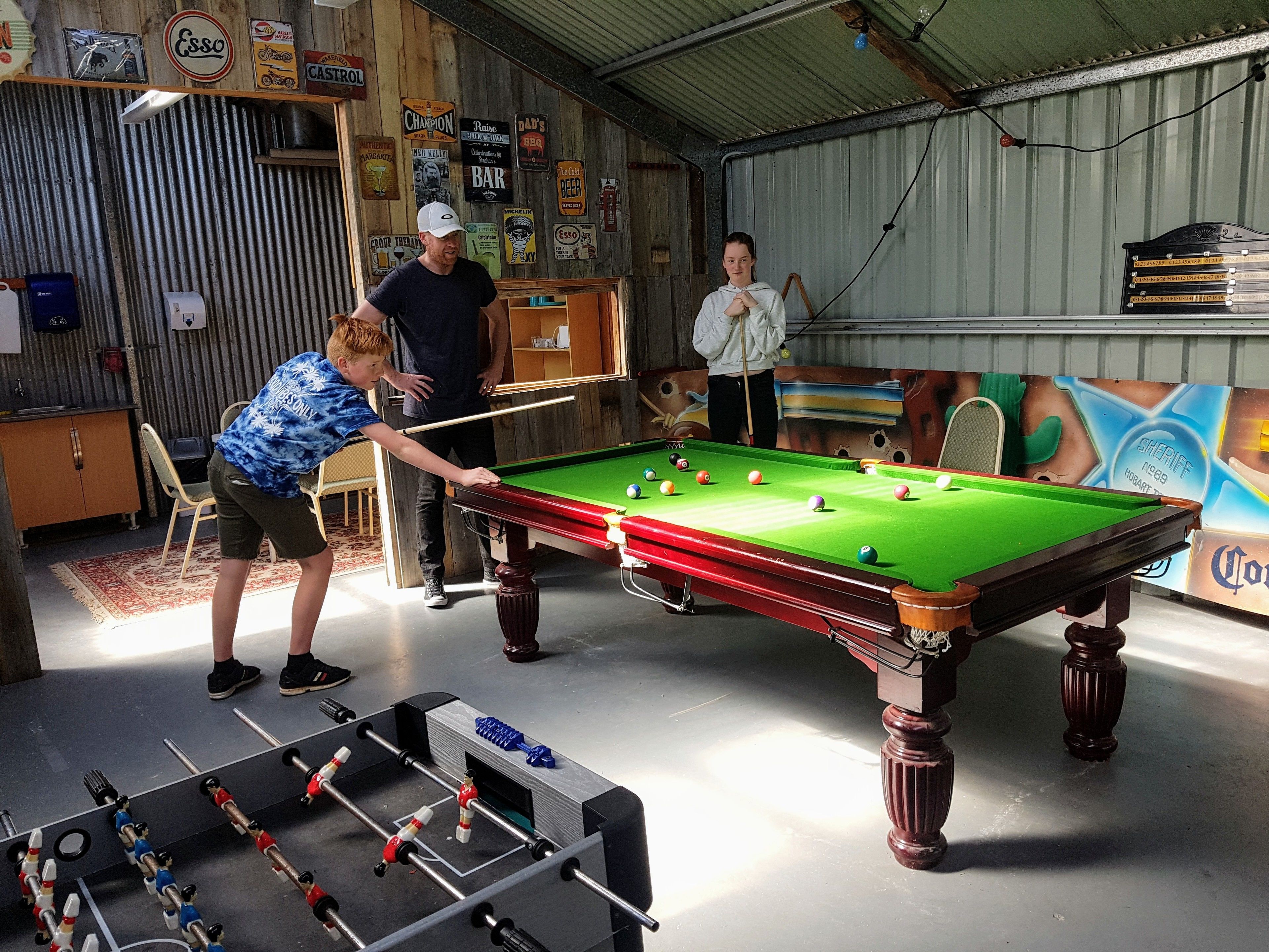 A billiards table in a room with a rustic decor, including a foosball table and various wall signs.