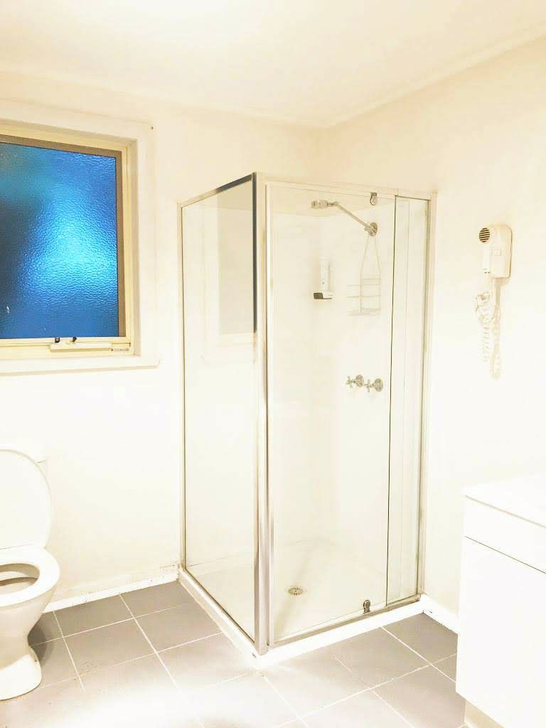 Un baño con cabina de ducha de vidrio, inodoro y ventana con vista al mar.