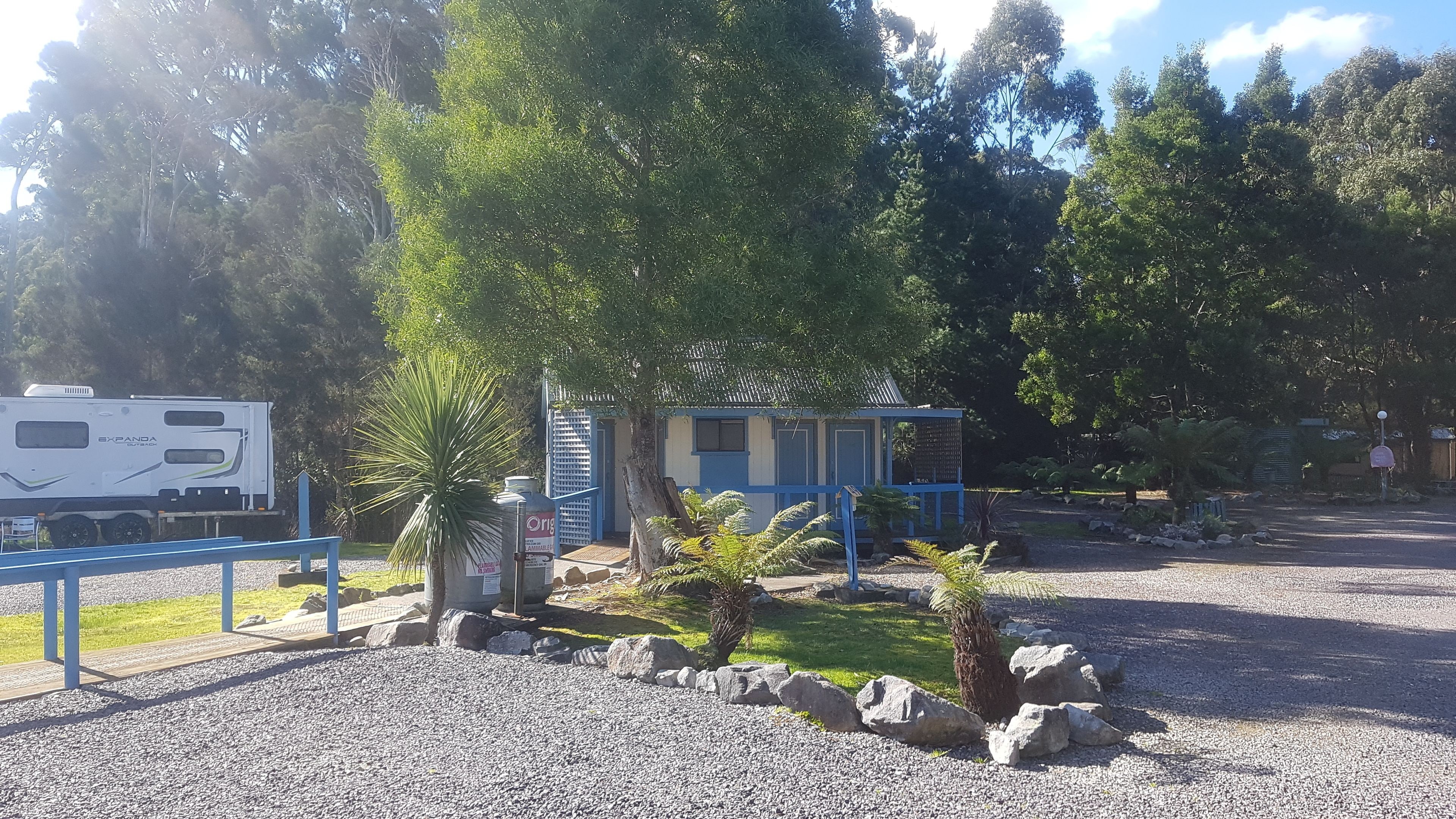 A small building with a blue roof, surrounded by a gravel area with rocks and small plants.