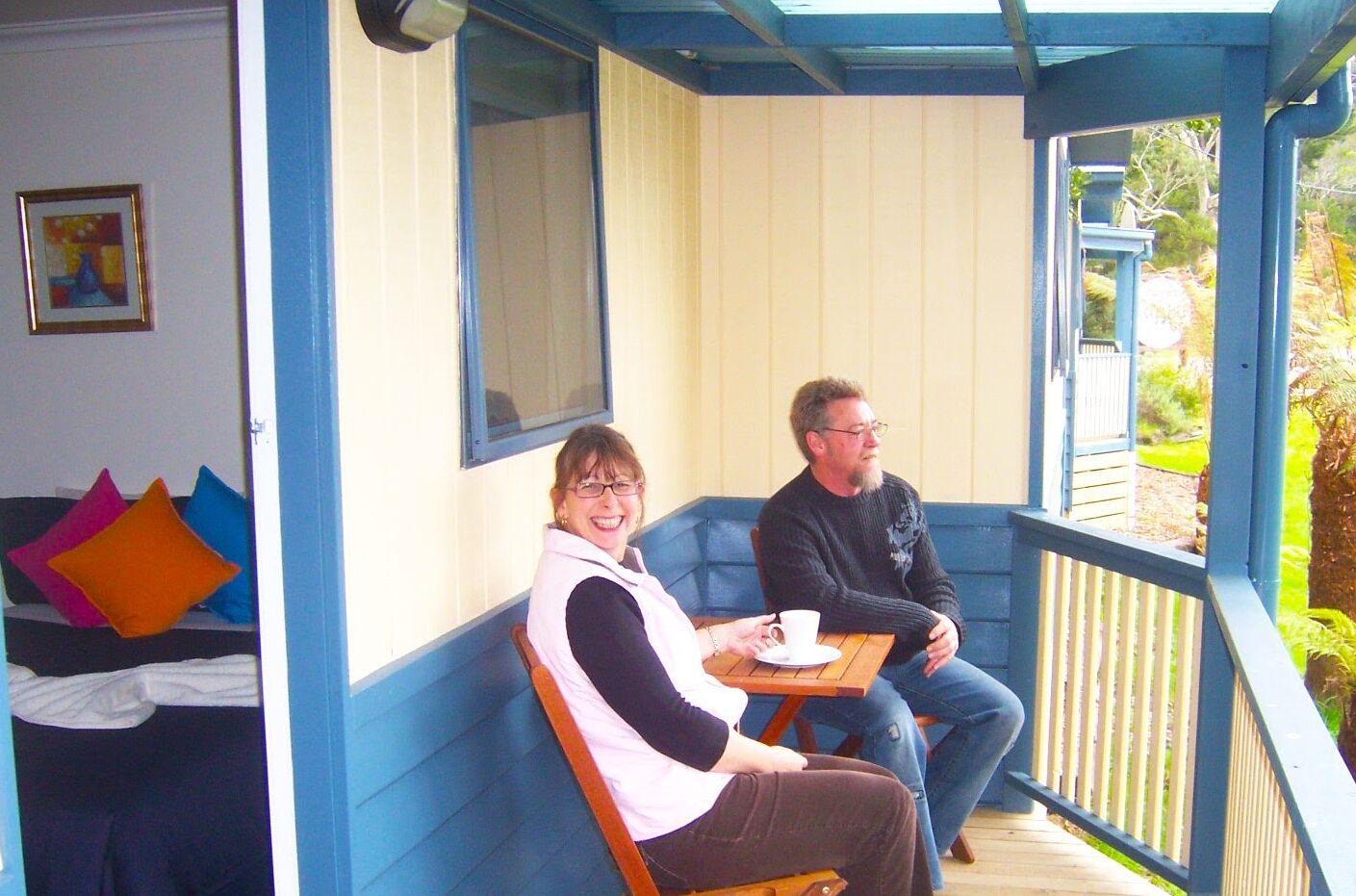 Two people seated at a table on a covered porch with a view of greenery.