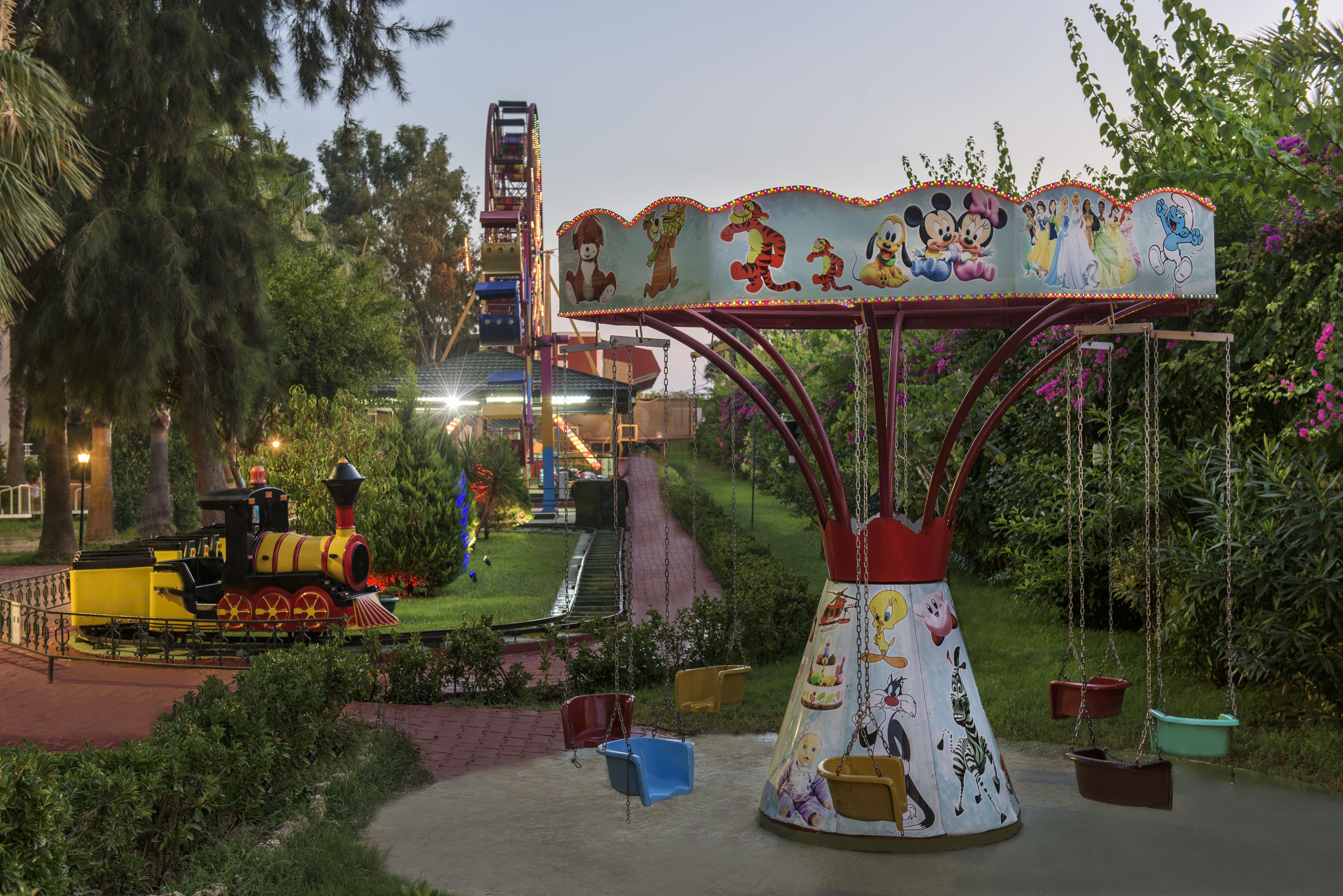 A carousel with cartoon characters, a small train, and a roller coaster in the background.