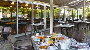 Ein Straßencafé mit Tischen und Stühlen, beschattet durch ein Markisenvorzelt, und ein reichhaltiges Frühstücksbuffet auf dem Tisch.