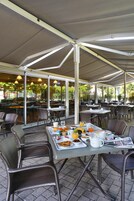 An outdoor cafe with tables and chairs, covered by a canopy, and a breakfast spread on the table.