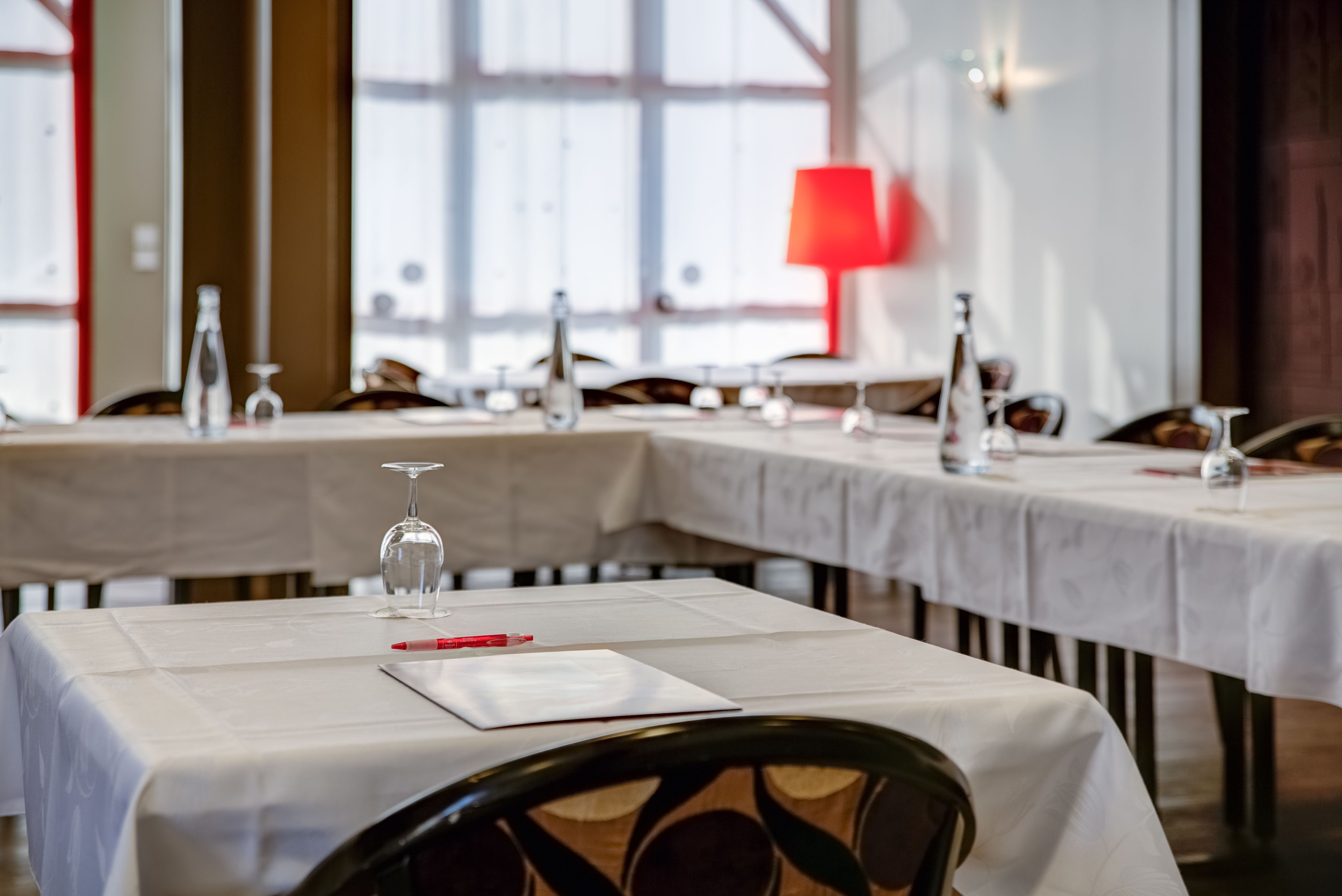 A restaurant with tables set for dining, featuring white tablecloths and wine glasses.