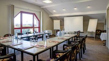 A conference room with long tables, chairs, a projector screen, and a large window with a view.
