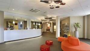 Ein moderner Empfangsbereich mit einer gebogenen weißen Theke, mehreren Pendelleuchten und einer Sitzecke mit orangefarbenen Sofas und roten Hocker.